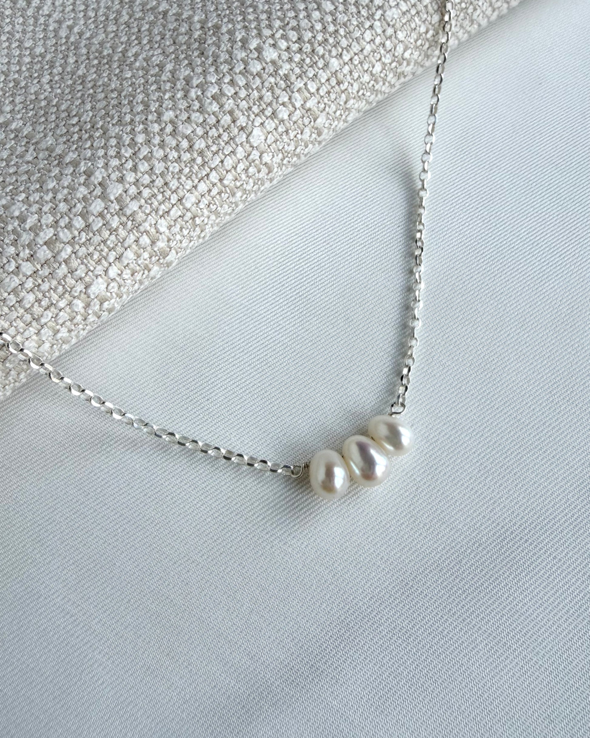 Minimalist pearl necklace featuring three dangling freshwater pearls on a fine chain in sterling silver or gold filled, resting around the collarbones.